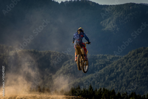 Motocross rider jumping in the air. Alps mountains in background. Dirt track on a sunny late summer day. High speed photography