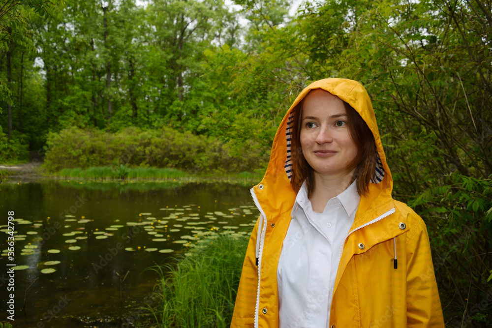 A young girl stands near a swamp in a yellow hooded jacket