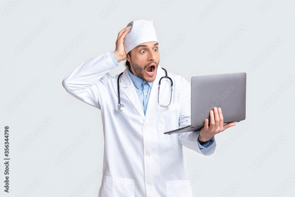 Shocked young doctor looking at laptop in amazement