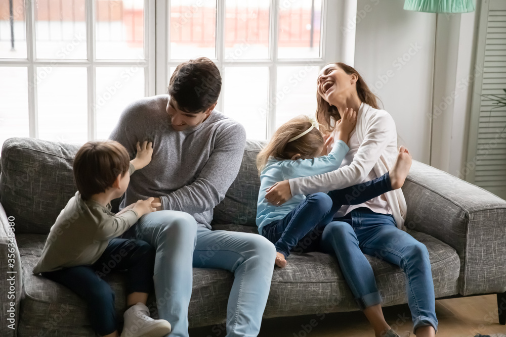 Overjoyed young Caucasian family with little preschooler kids relax on couch at home have fun tickling, happy parents with small children play together in living room engaged in funny game activity Overjoyed young Caucasian family with little preschooler kids relax on couch at home have fun tickling, happy parents with small children play together in living room engaged in funny game activity