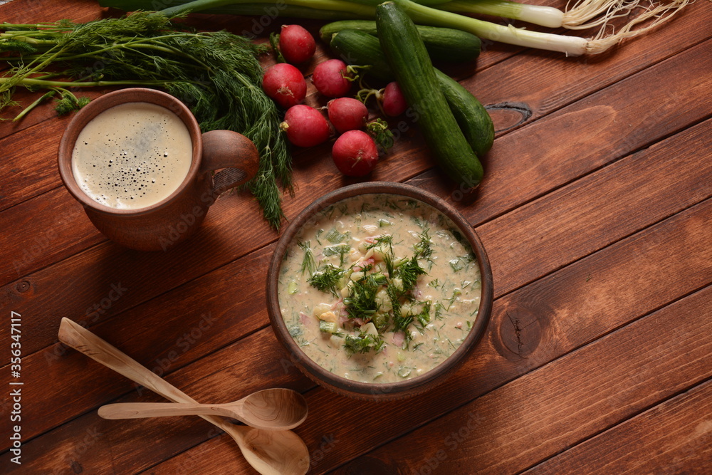Fototapeta Russian cuisine- Okroshka, Summer light cold yogurt soup with cucumber, radish, eggs and dill with sour cream and green onion on a wooden table.