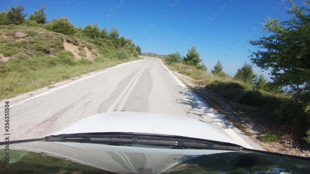 Car driving point of view. Moving uphill on a mountain road in the southern European countryside on a bright sunny day.