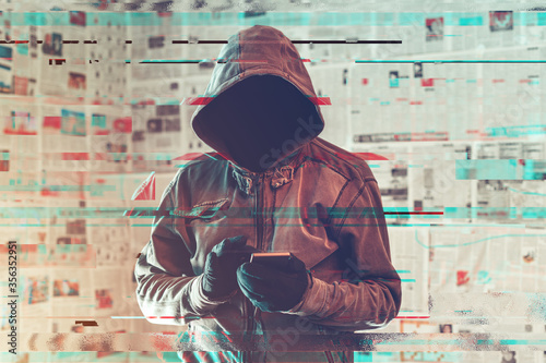 Hooded hacker person using smartphone in infodemic concept photo