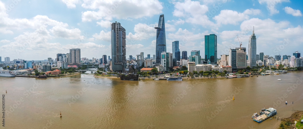 Fototapeta premium Aerial view of Bitexco Financial Tower building, train tracks, buildings, roads, and Saigon river in Ho Chi Minh city. High quality panorama image