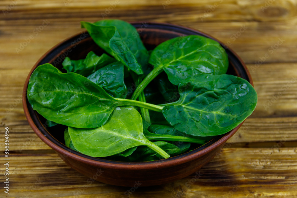 Fresh green spinach leaves in bowl on a wooden table
