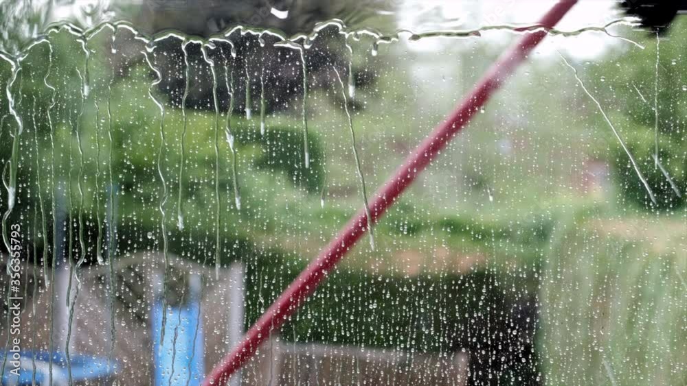 A house window being cleaned and washed by a water fed brush system on a long pole.