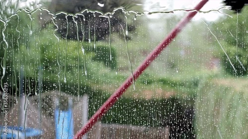 A house window being cleaned and washed by a water fed brush system on a long pole.
