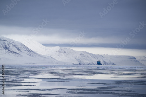 Melting sea ice in the Arctic on Spitsbergen on a cloudy day with mountains with s ship at the horizon © Sandra