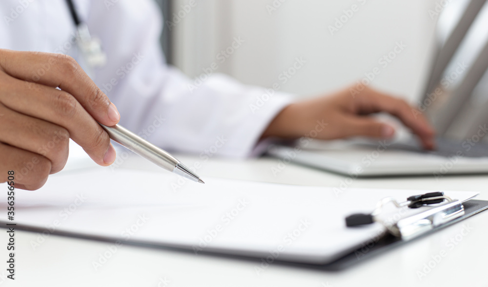 Doctor uses a laptop computer to record patient information and write it on a document to prepare for diagnosis in the room of a modern hospital, Emergency assistance and health care concept. Doctor uses a laptop computer to record patient information and write it on a document to prepare for diagnosis in the room of a modern hospital, Emergency assistance and health care concept.