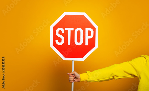 Stop sign. Girl in a yellow hoodie showing only her hand with "stop" sign.