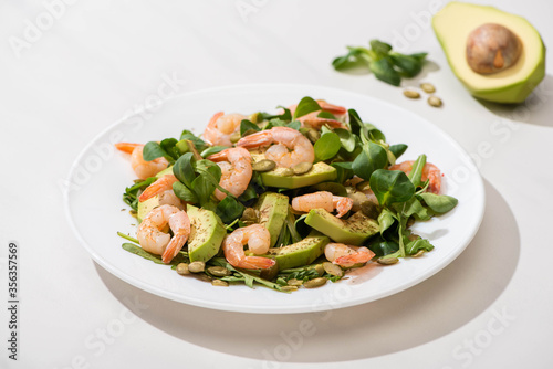 selective focus of fresh green salad with shrimps and avocado on plate on white background