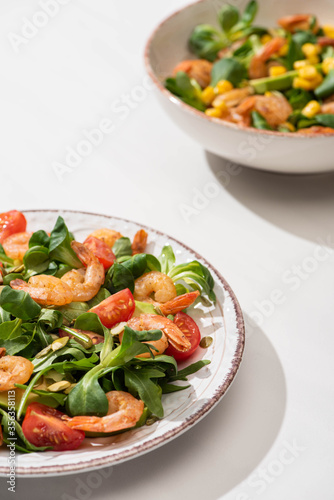 selective focus of fresh green salad with shrimps and avocado on plates on white background