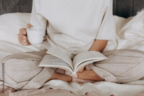 girl pajamas reads book holds cup tea