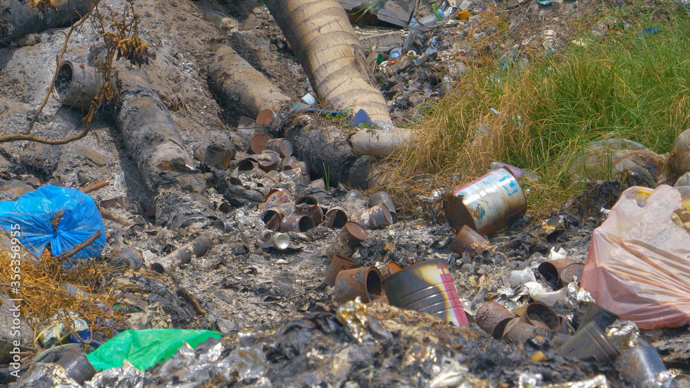 CLOSE UP: Half-burnt garbage is scattered around a meadow on an exotic island.