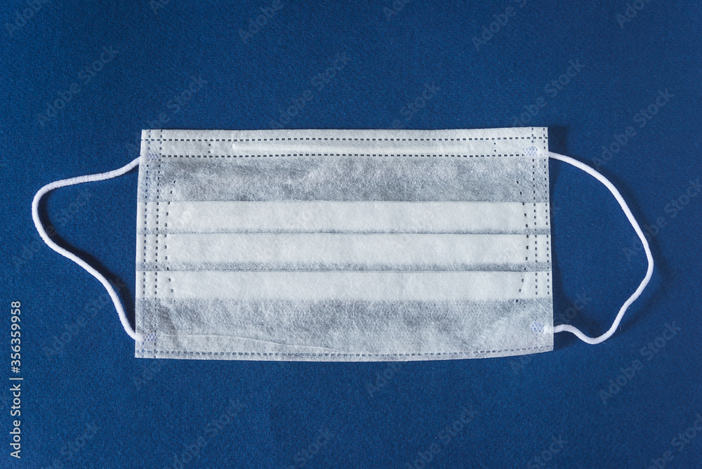 Illness prevention concept. New White medical protective mask on blue background Illness prevention concept. New White medical protective mask on blue background