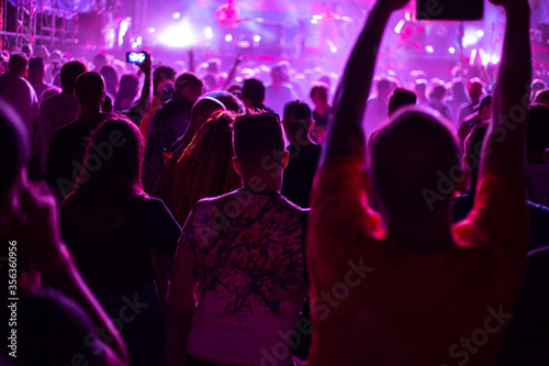 crowd of fans at a rock music concert, young people in the club illuminated by spotlights shoot videos on the phone, leisure and entertainment