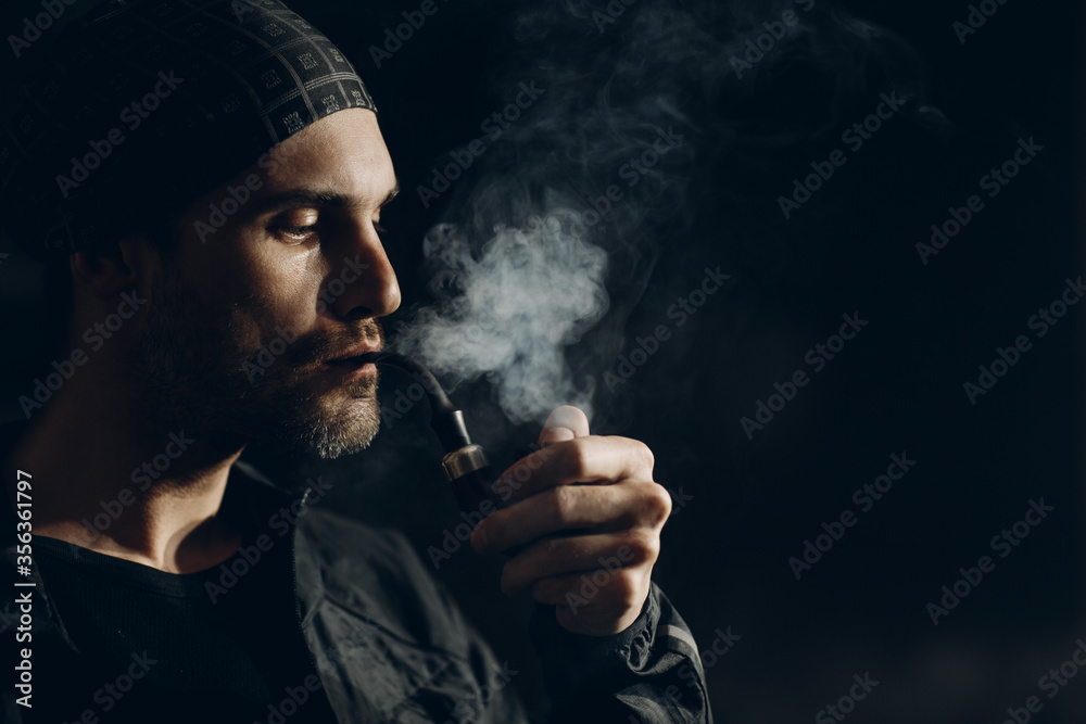 Man smoking a pipe on dark background. Profile portrait. Man smoking a pipe on dark background. Profile portrait.