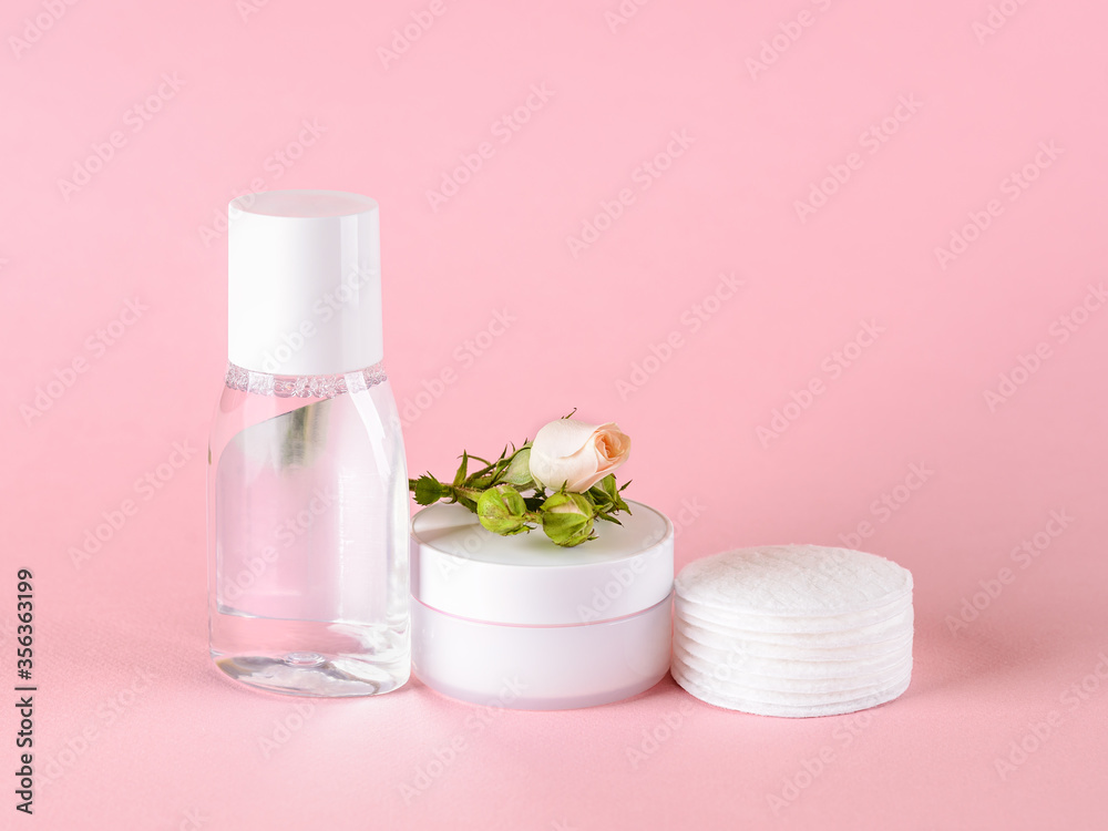 Skin tonic lotion or micellar water, facial cream, cotton pads and small rose on a pastel pink background. Cosmetics for moisturizing and cleansing. Skin, hair or body care.