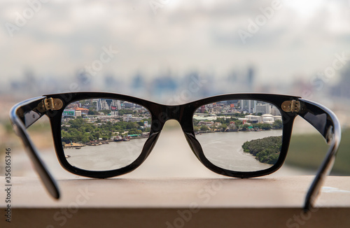 Fototapeta Naklejka Na Ścianę i Meble -  Black eyeglass on a reflective surface. View through the lens of glasses that look at the Chao Phraya River.