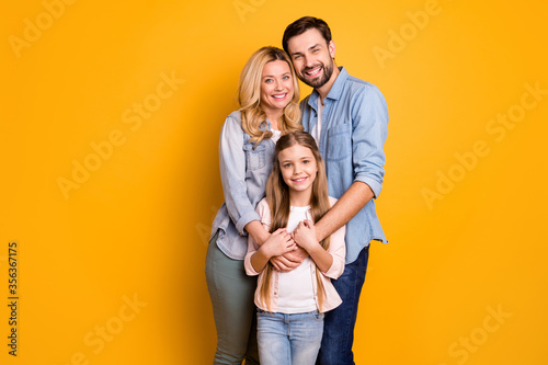 Photo wife beautiful mother lady handsome husband dad guy couple hug hold little school girl daughter happy together wear casual shirts clothes isolated yellow color background © deagreez