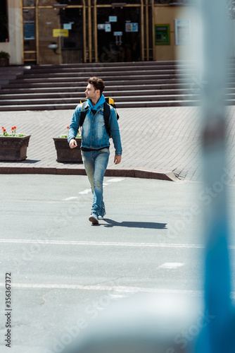 Selective focus of courier with backpack walking on road crosswalk