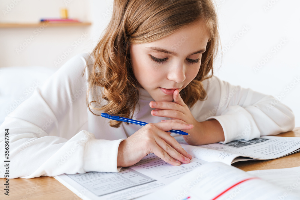 Photo of focused girl writing in exercise book while doing homework Photo of focused girl writing in exercise book while doing homework