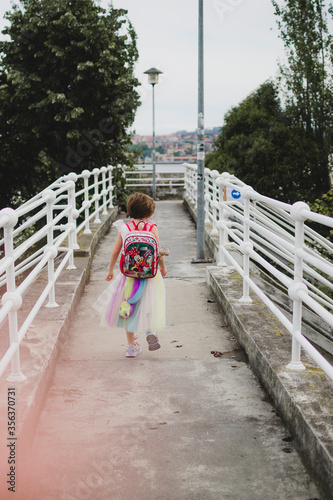 Niña de espaldas andando por un puente con disfraz y mochila