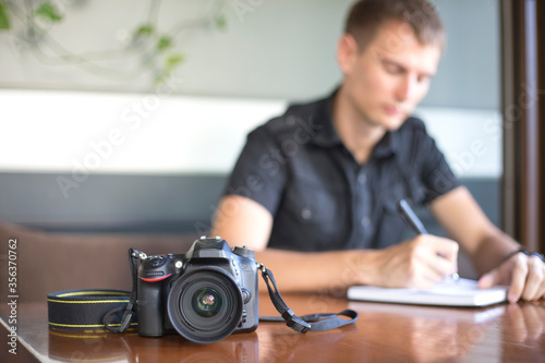 Digital camera lies on table on the background of photographer writing orders in notebook
