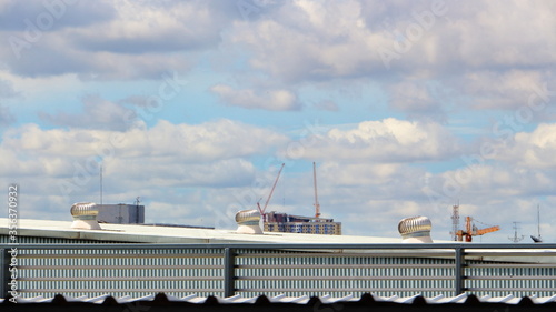 Roof ventilator On the factory roof In the heat Behind the construction crane White clouds and blue sky