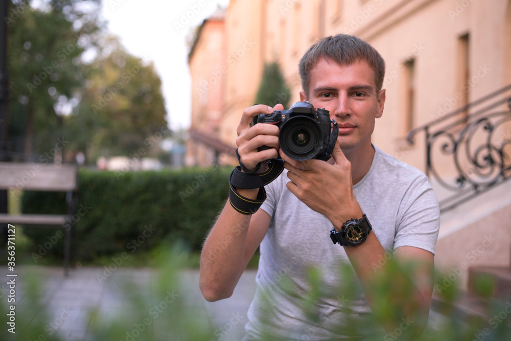 Portrait of young man photographer with digital SLR camera who takes pictures in the park