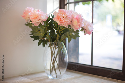 Fototapeta Naklejka Na Ścianę i Meble -  Pink peonies stand in a glass vase on a windowsill