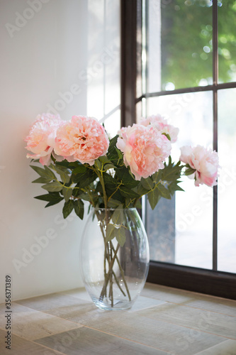 Fototapeta Naklejka Na Ścianę i Meble -  Pink peonies stand in a glass vase on a windowsill, vertical orientation