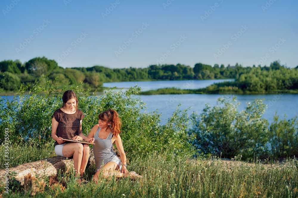 Two young women have a rest on a sunny day in nature and read a book.