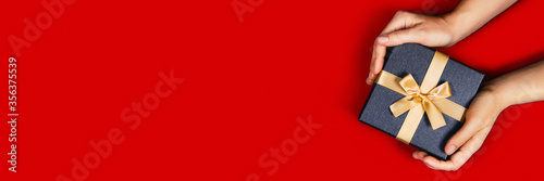 Web banner with women's hands holding a box with a gift or surprise on a red background.