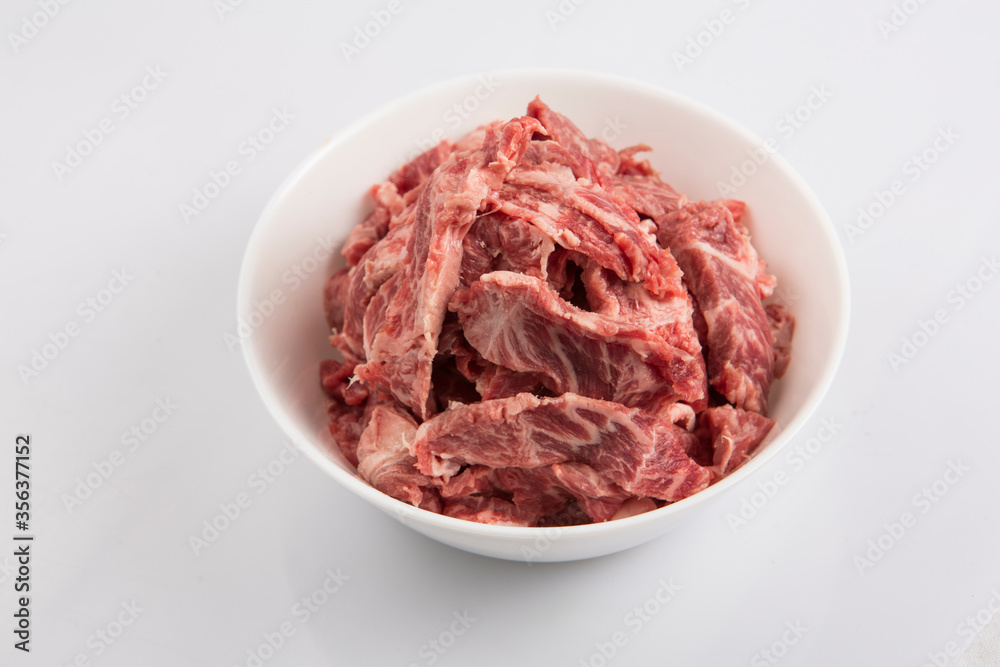 isolated close up top view shot of sliced raw beef fillet pieces in a white bowl on a white background