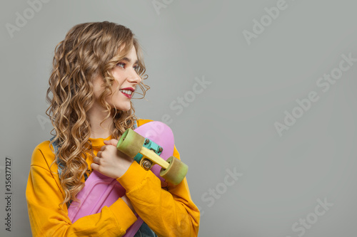 Young woman in yellow sweatshirt holding skateboard on gray background