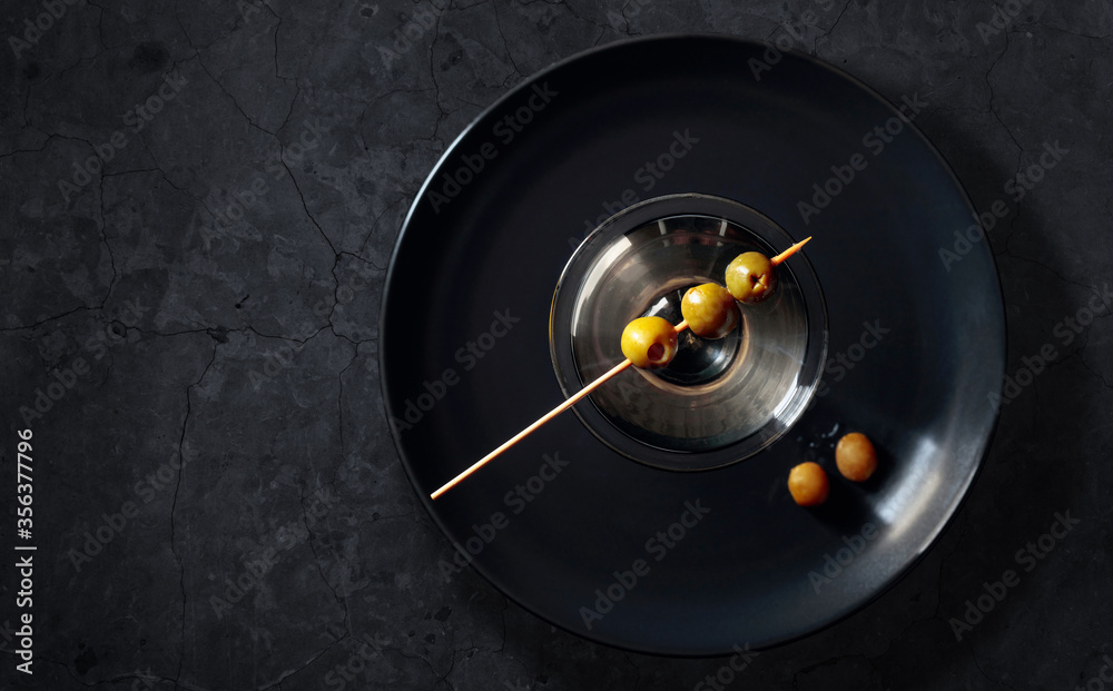 Obraz premium Dry martini with green olives on a black stome table.
