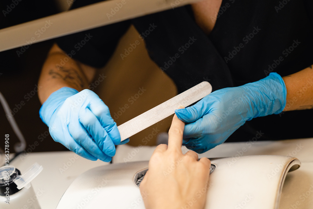 Aesthetician doing the manicure, filing the nails with a file to his client in a beauty center Aesthetician doing the manicure, filing the nails with a file to his client in a beauty center
