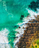 Top down aerial view of a beach with waves, rocks and sand.