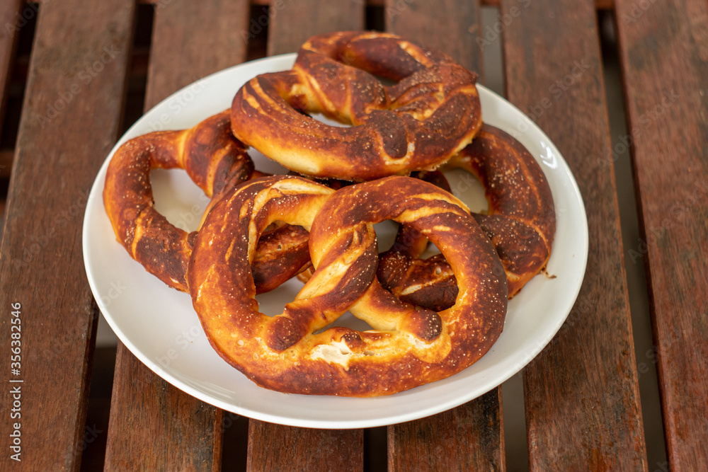 Simple traditional salted home made Pretzel on a white plate set on brown wooden boards top view Simple traditional salted home made Pretzel on a white plate set on brown wooden boards top view