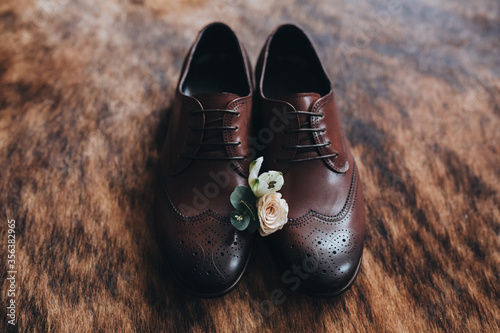 Wedding accessories. Boutonniere of flowers lies on men's leather shoes