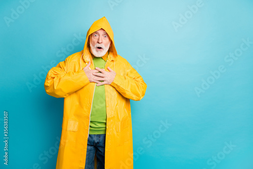 Portrait of his he nice attractive frightened amazed grey-haired man wearing yellow coat cyclone news reaction heart attack isolated on bright vivid shine vibrant blue color background