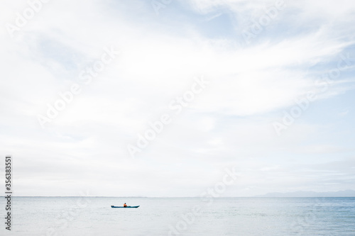 A man using a blue Kayak in the Ocean on a still but cloudy day