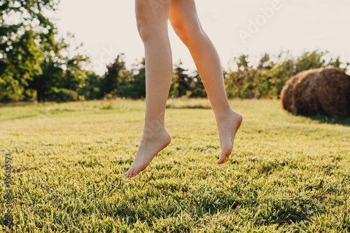 Close-up of barefoot legs of young woman in the park, jumping on green grass.