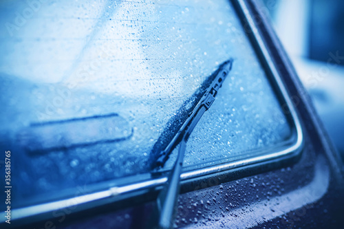 The rear window of the car and the black windshield wiper are covered with drops of heavy rain in cloudy dark weather. Bad weather. 