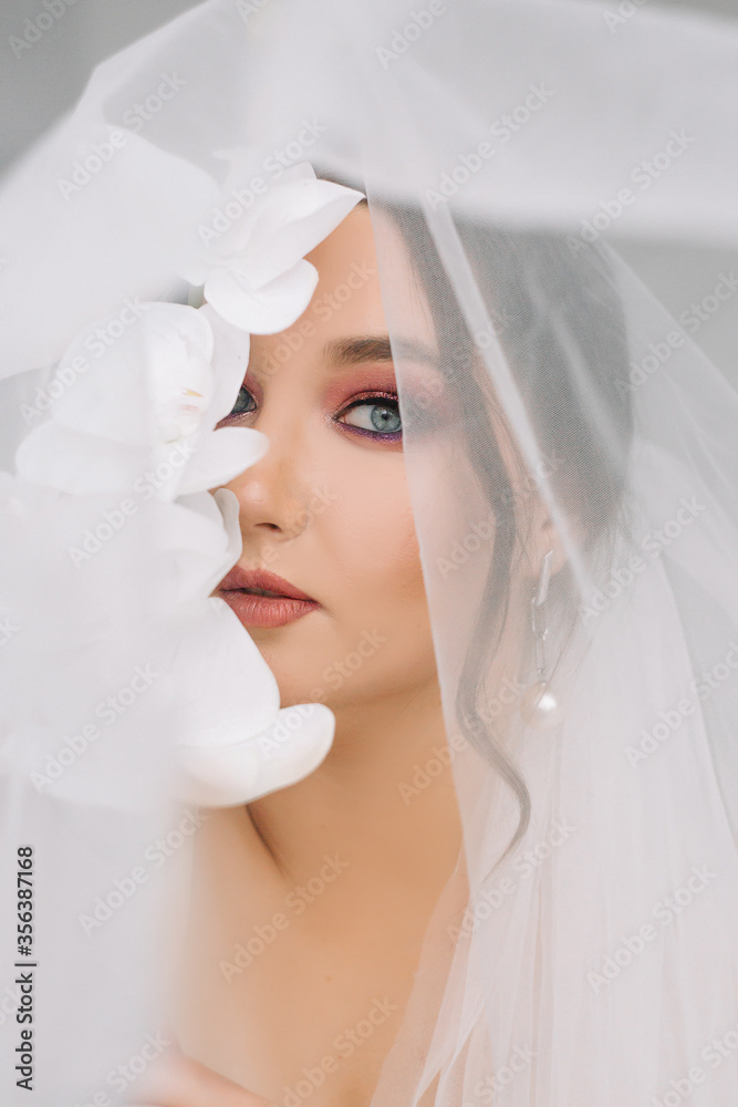 Amazing model girl bride with bright makeup looks at the camera. Portrait. Bride portrait with bright makeup and orchid
