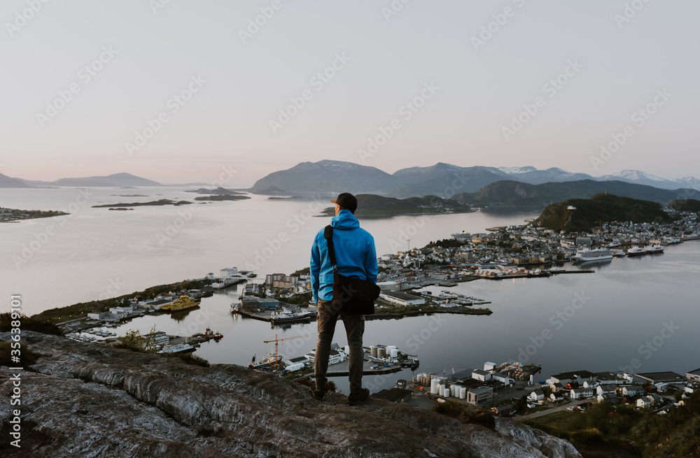Hiker is looking at the norwegian city from the cliff. Travel and hiking concept