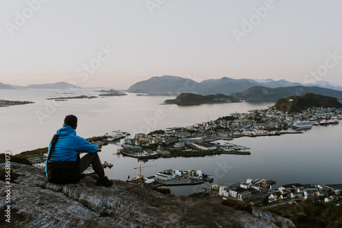 Solitary traveller is looking at the norwegian city from the cliff. Travel and hiking concept