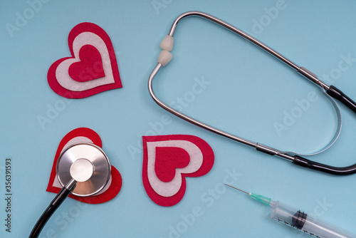 Medical tool stethoscope with a syringe with hearts on a blue background, close-up.