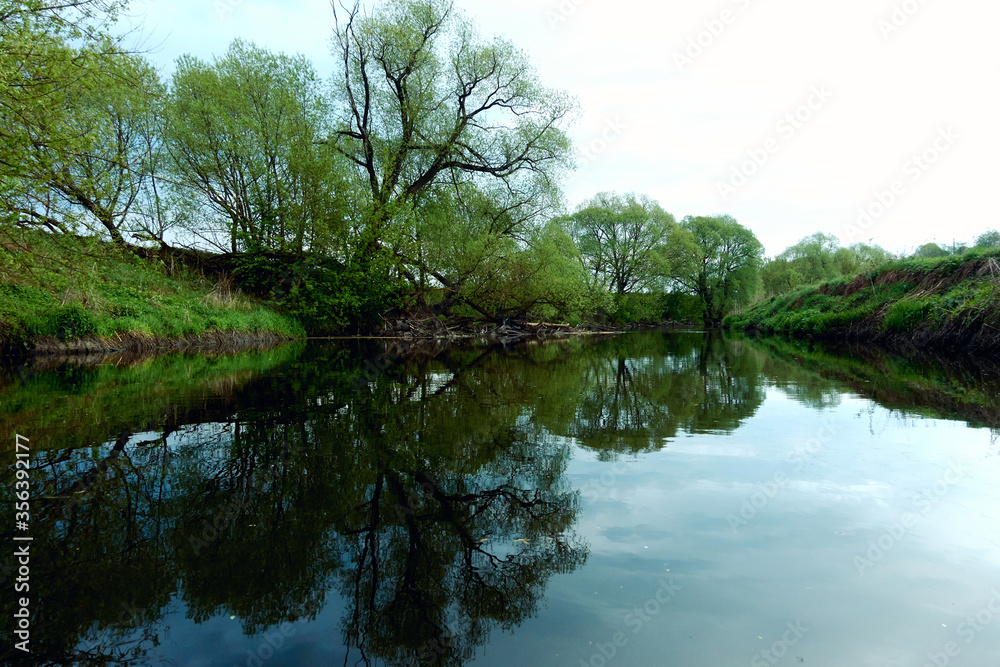 Reflection of green trees and banks in a calm river in the summer. River rafting in summer. Packrafting in wilderness. Reflection of green trees and banks in a calm river in the summer. River rafting in summer. Packrafting in wilderness.
